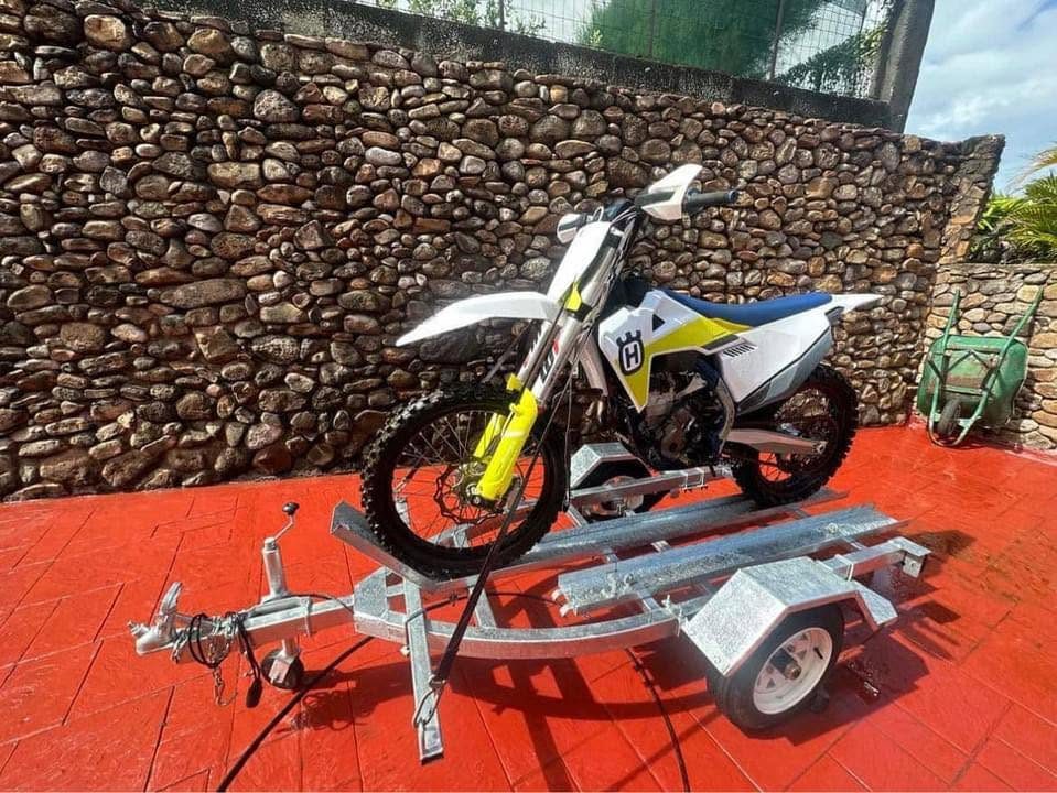 Remorque moto galvanisée chargée d'une moto cross, devant un mur en pierre